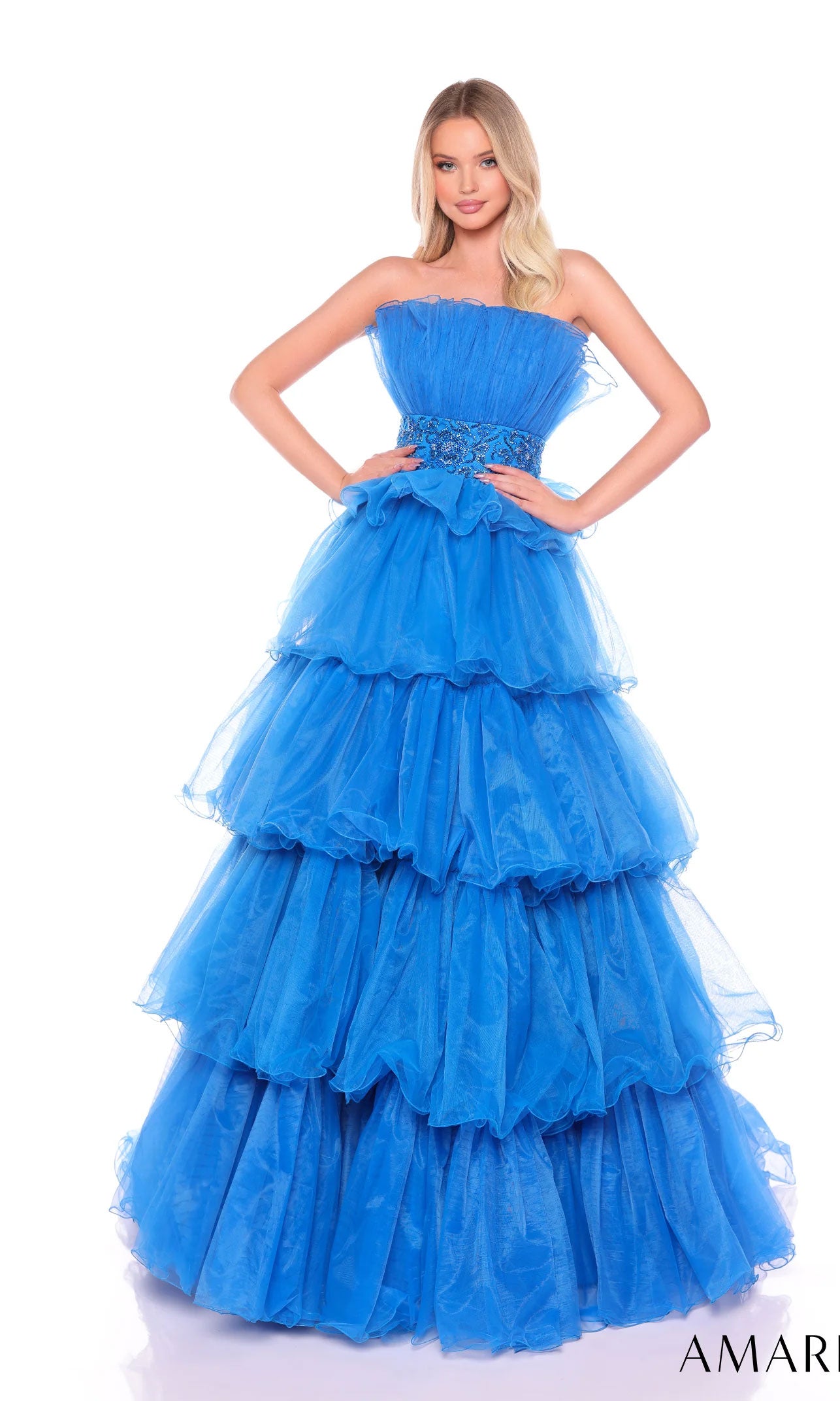 A woman stands against a white background wearing the Long Formal Dress 88083 by Amarra, a blue strapless ball gown with a beaded waist and floor-length tiered ruffled tulle layers.